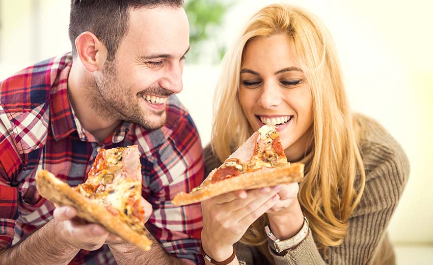 Mann und Frau essen Pizza aus dem Pizzamaker und haben jeweils ein Stück davon in der Hand