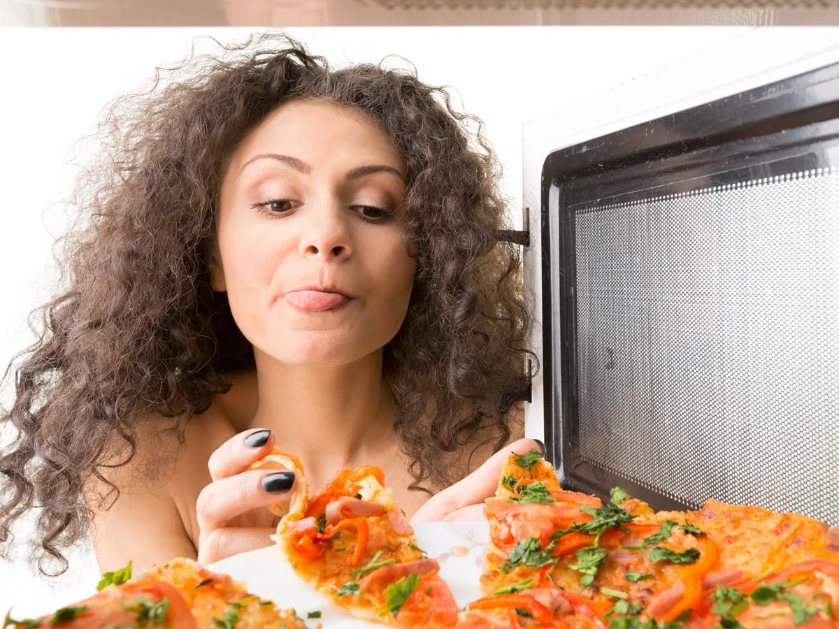 Frau nimmt eine STück Pizza aus dem Pizzabackofen