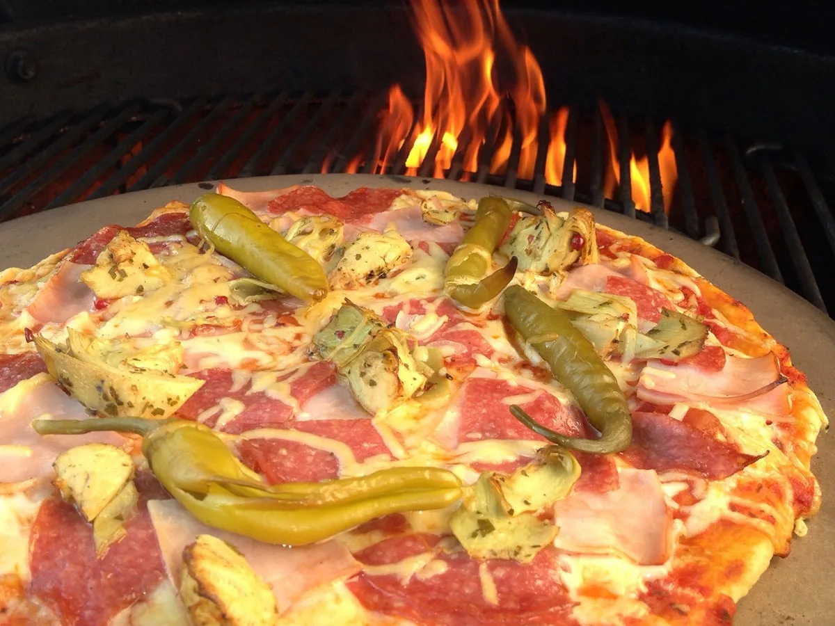 Frische Pizza auf einem Pizzastein von Weber auf einem heißen Grill