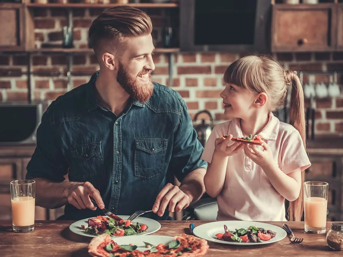 Vater mit Tochter isst eine leckere Pizza am Küchentisch. Mit dem Pizzaofen Alfredo von Bestron geht das ganz einfach.